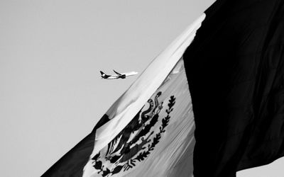 Low angle view of mexican flag against airplane and sky on sunny day