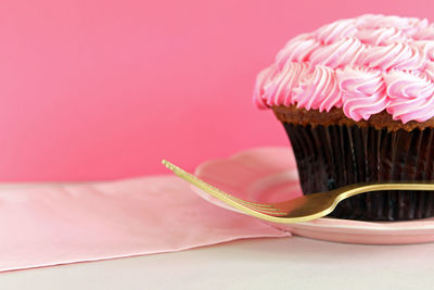 Close-up of cupcake with fork in plate on table against pink wall
