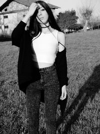 Young woman looking away while standing on grassy field during sunny day