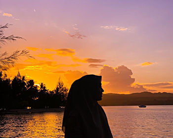 Silhouette woman by lake against sky during sunset