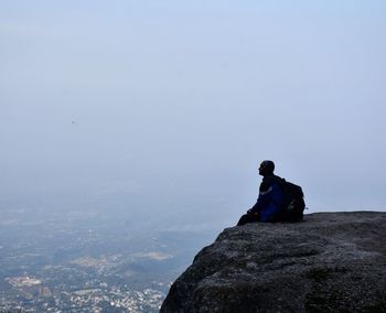 Man sitting on rock formation against sky