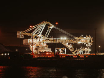 Illuminated pier by river against sky at night