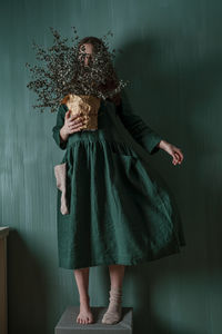 A young woman in a green linen dress making her creative self-portrait against a green wall