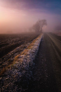 Road amidst field against sky during sunset