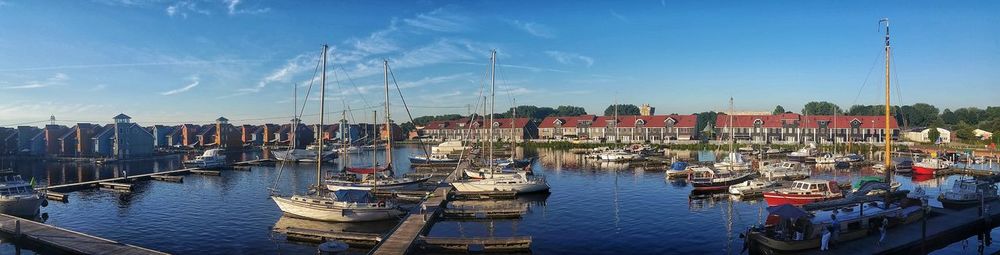 Panoramic view of boats moored at harbor by buildings against sky