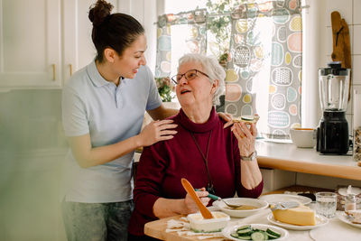 Retired senior woman eating breakfast while talking with female volunteer at nursing home