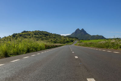 Road leading towards mountains against clear sky