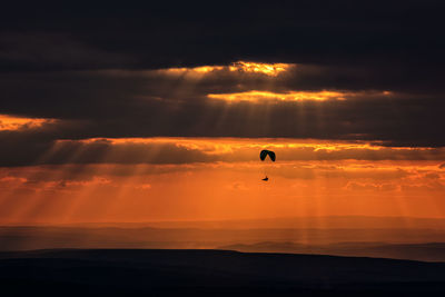 Silhouette person paragliding over sea against sky during sunset