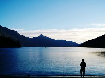 Silhouette man standing on lake against sky