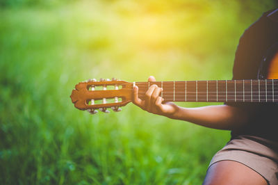 Cropped hand of person playing guitar over field