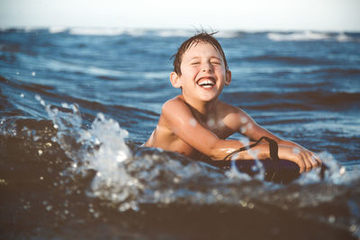 Shirtless smiling boy bodysurfing in sea