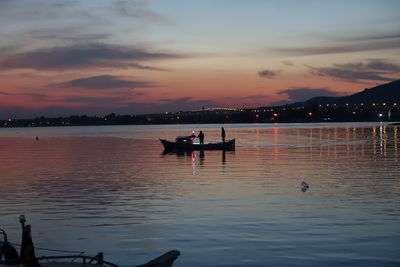 Silhouette people in sea against sky during sunset