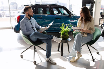 Salesman sitting with female customer in car showroom