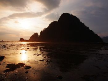 Silhouette rocks on beach against sky during sunset