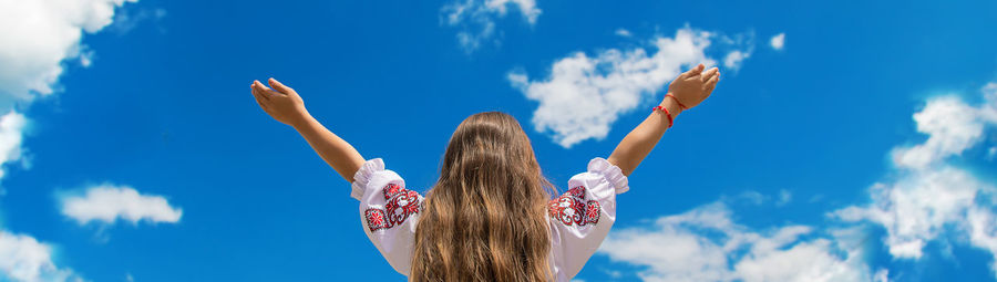 Rear view of girl with arms raised against sky