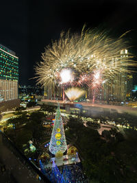 Firework display over illuminated city against sky at night