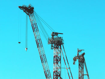 Low angle view of cranes against clear blue sky