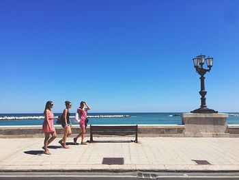 People on sea shore against clear blue sky