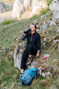 Woman sitting on a rock while having a break and drinking during hiking.