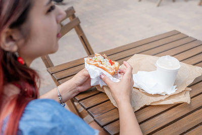 Closeup of woman hands holding hamburger, woman eating fast food at street cafe, view from behind