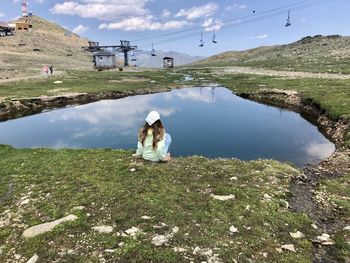 Rear view of woman sitting by lake against sky