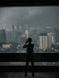 Silhouette man taking photograph of city while standing against glass window