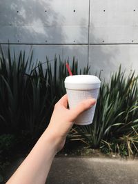 Cropped hand of person holding coffee cup against wall outdoors