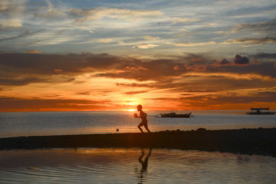 Silhouette person standing on beach against sky during sunset