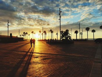 Silhouette people walking on street against sky at sunset