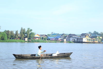 Man rowing boat in lake against sky