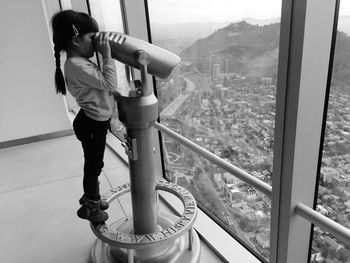 Side view of girl looking at cityscape through coin-operated binoculars