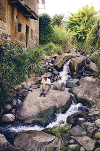 Man weaving basket while sitting on rock