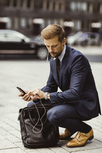 Male entrepreneur looking at time while crouching on street