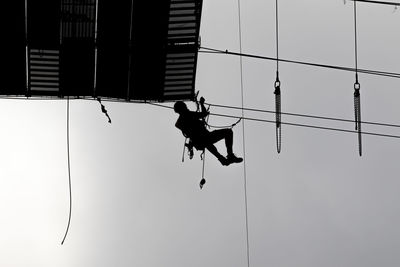 Low angle view of silhouette man hanging on rope against clear sky