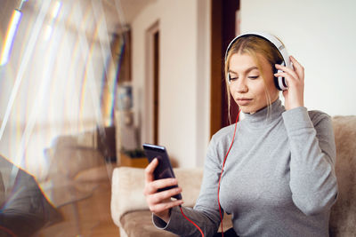 Young woman using smart phone while sitting on laptop