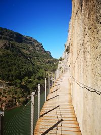 Footpath leading towards mountains against clear blue sky