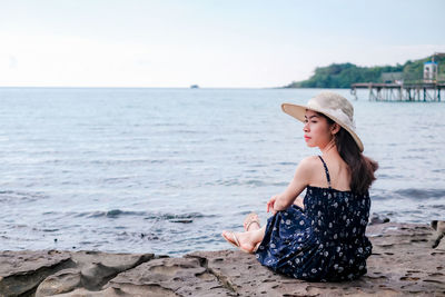 Woman sitting on beach by sea against sky