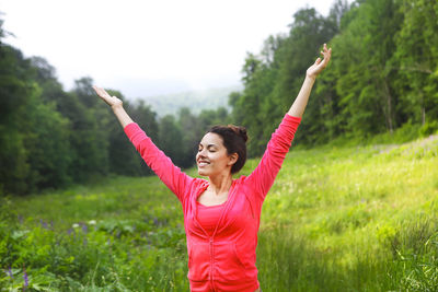 Happy young woman with arms raised on grass