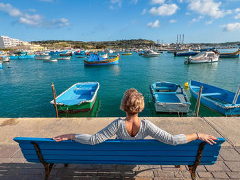 Rear view of woman sitting on bench against sky