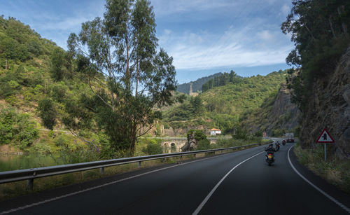 Road by trees on mountain against sky