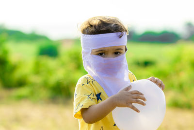 A small child with white swollen balloon in both hands and wear home made face mask 