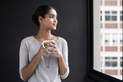 Smiling female interior designer holding coffee mug while looking through window in office