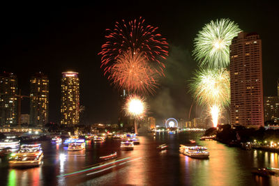 Firework display over illuminated city against sky at night