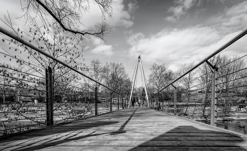 Bare trees on footbridge against sky