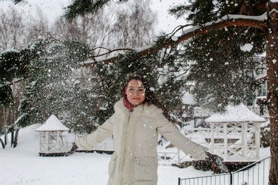 Young woman throwing snow while standing on land during winter