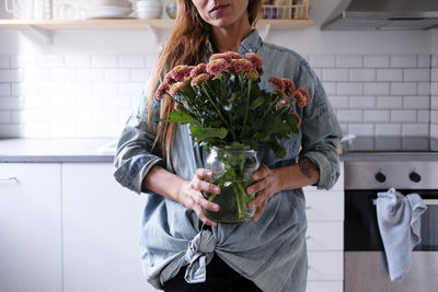 Midsection of woman carrying flower vase while standing at kitchen