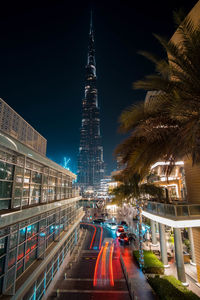 Light trails on road amidst buildings against sky at night