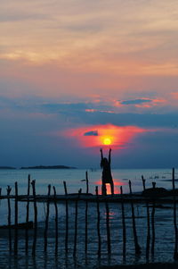 Silhouette woman with arms raised standing on pier over sea against sky during sunset