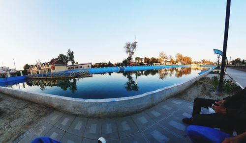 Reflection of man photographing in swimming pool against sky