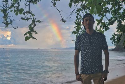 Portrait of young man standing at beach against sky